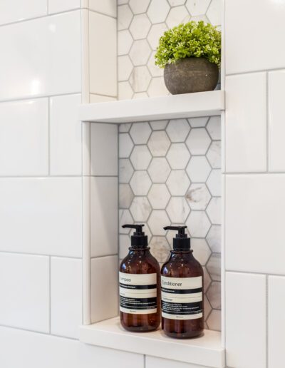 A white tiled shower with shelves and soap dispensers.