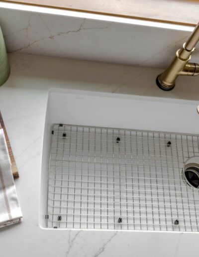 A modern kitchen sink featuring a metal grid, with a wooden cutting board and striped towel nearby, complemented by a brass faucet.