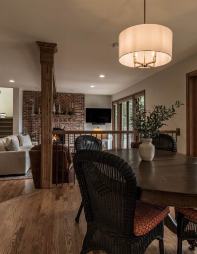 Modern living room with wooden floors and furniture, a large dining table, and open views to adjoining rooms, featuring warm lighting and a serene ambiance.