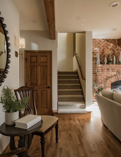 Cozy living room with a brick fireplace, a staircase, wooden furniture, and decorative plants.