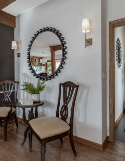 Elegant hallway featuring two chairs, a round mirror, built-in shelves, and a fireplace, with natural light filtering through windows.