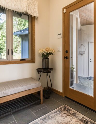 A cozy entryway featuring a bench, floor mat, large window, and a wooden door leading to another room.