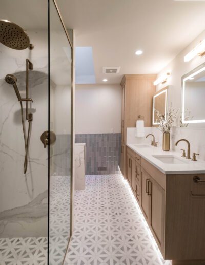 Modern bathroom with marble walls, glass shower enclosure, wooden cabinets, and geometric floor tiles.