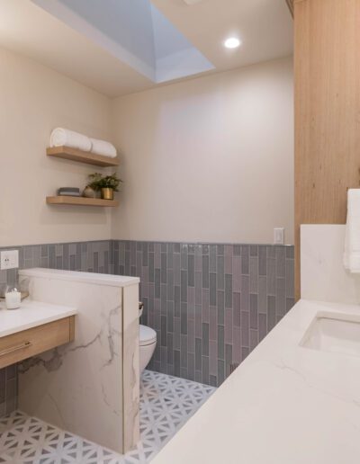 A modern bathroom with wooden cabinets, a marble countertop, an undermount sink, wall-mounted mirror, and gray tile accents.