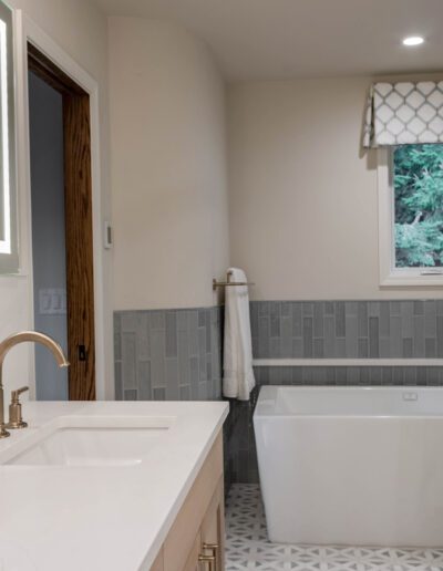 Modern bathroom featuring a dual sink vanity with marble countertop, freestanding bathtub, glass shower stall, and a window with a view of greenery.