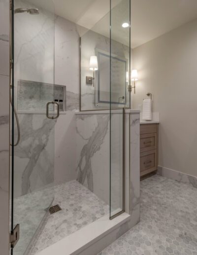 A modern bathroom with marble walls and flooring, featuring a glass-enclosed shower and a wooden vanity.