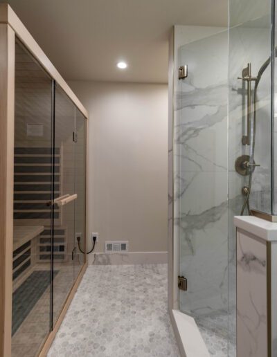 A modern bathroom featuring a glass shower stall next to a wooden sauna, with marble walls and hexagonal floor tiles.