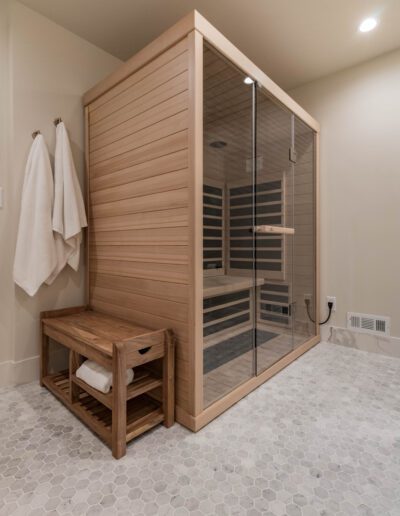 Modern bathroom featuring a wooden sauna with glass doors and a bench, tiled flooring, and white towels hanging on the wall.