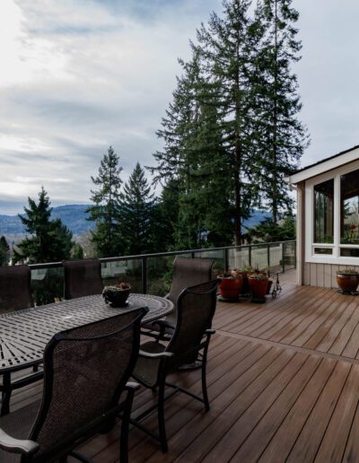 Spacious wooden deck of a house with outdoor furniture overlooking a scenic landscape with trees and distant hills.