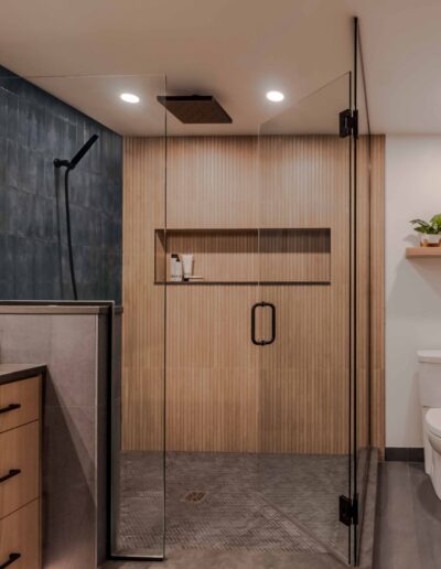 Modern bathroom featuring a glass-enclosed shower with wooden panel accents and black fixtures, a toilet, and a wooden vanity with drawers.